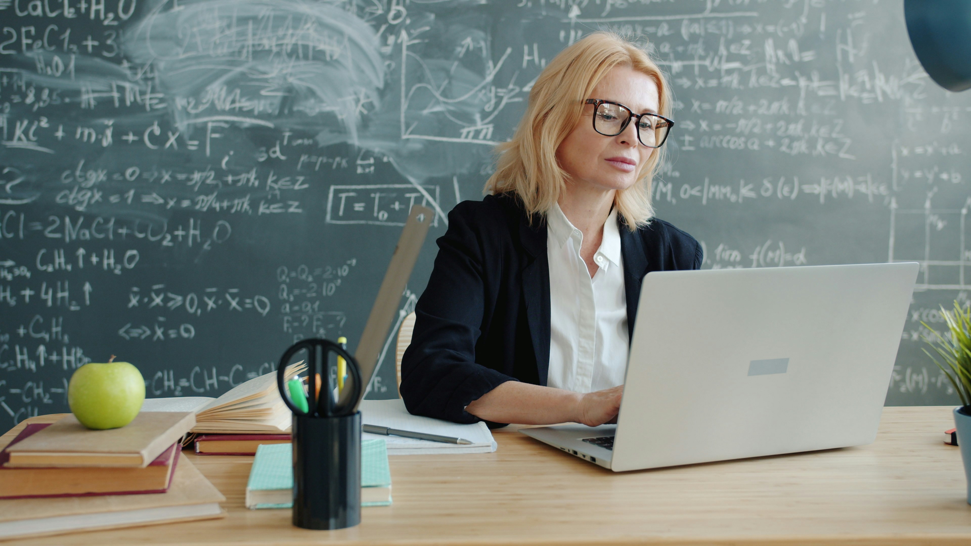 Teacher working on laptop in front of chalkboard
